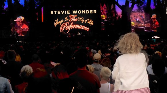 young girl on parents shoulders watching Stevie Wonder gig