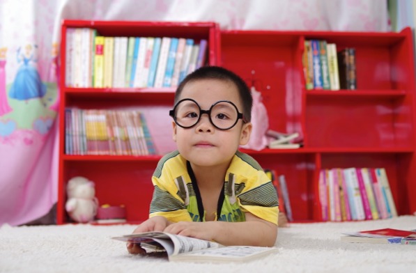 cute little Asian Boy with glasses on a rug reading a book - Maggie & Rose Life