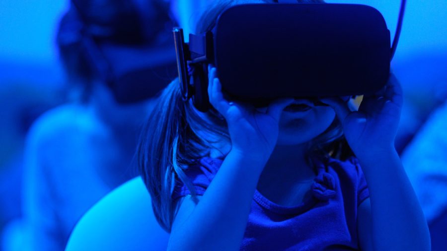 Small girl holding a VR headset to her face in a blue room