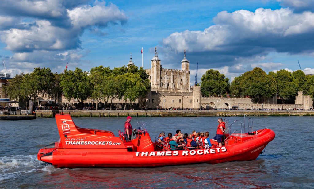 A red boat passing the tower of London on the river
