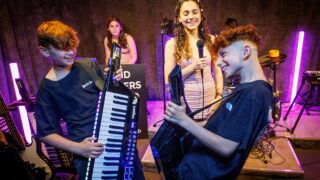 Boys playing keytars and girl singing in background
